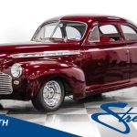 Mörkröd veteranbil, en coupe, parkerad i en studio med vita väggar.