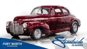 Mörkröd veteranbil, en coupe, parkerad i en studio med vita väggar.