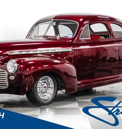 Mörkröd veteranbil, en coupe, parkerad i en studio med vita väggar.