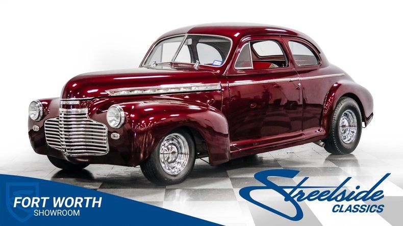 Mörkröd veteranbil, en coupe, parkerad i en studio med vita väggar.